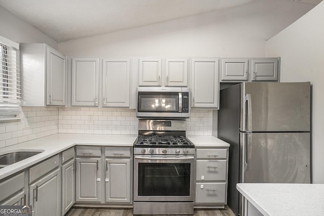 kitchen featuring gray cabinetry, lofted ceiling, stainless steel appliances, and hardwood / wood-style flooring