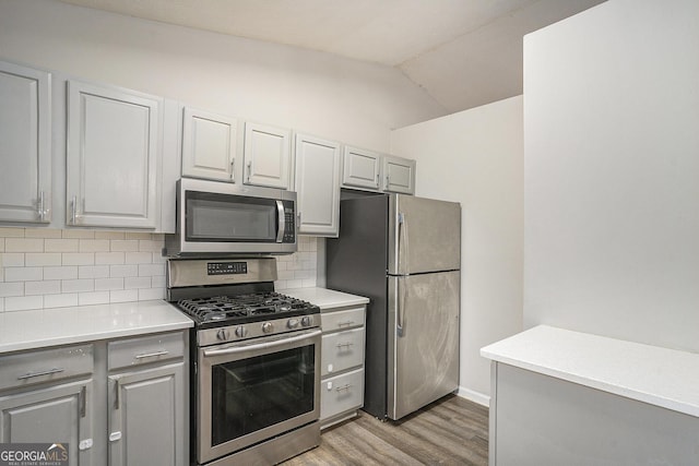 kitchen featuring lofted ceiling, light hardwood / wood-style flooring, decorative backsplash, gray cabinets, and appliances with stainless steel finishes