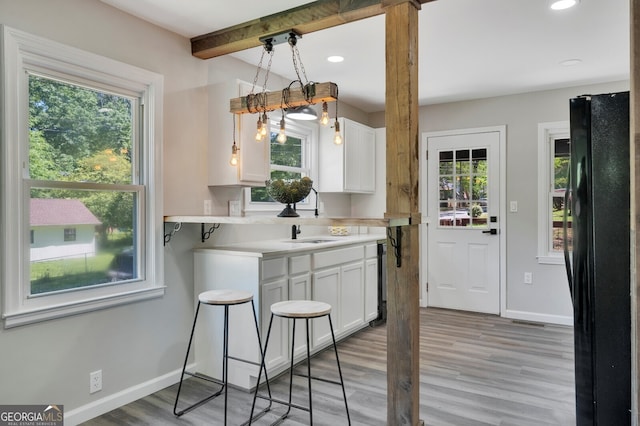 kitchen with plenty of natural light, black fridge, white cabinetry, and light hardwood / wood-style flooring