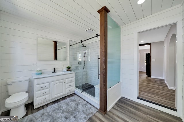 bathroom featuring wood-type flooring, toilet, wooden walls, vanity, and a shower with shower door