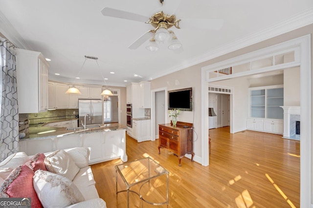 living room featuring a high end fireplace, sink, crown molding, light hardwood / wood-style flooring, and ceiling fan