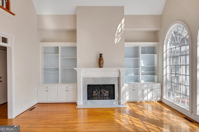 unfurnished living room with a high end fireplace, light hardwood / wood-style flooring, and lofted ceiling