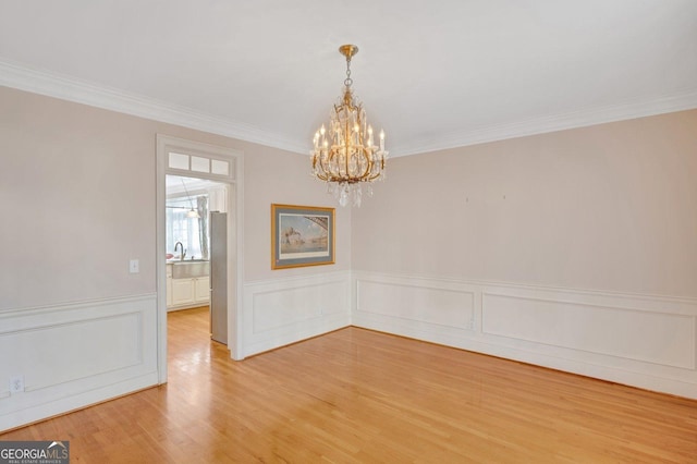 spare room with ornamental molding, a notable chandelier, and light wood-type flooring