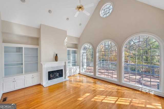 unfurnished living room with hardwood / wood-style flooring, a healthy amount of sunlight, a premium fireplace, and high vaulted ceiling