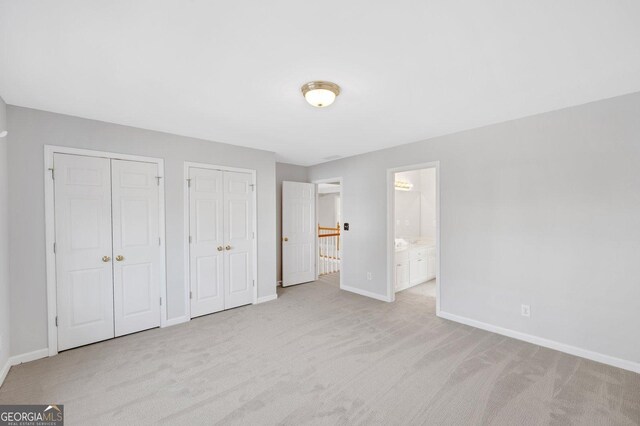 unfurnished bedroom with ensuite bathroom, light colored carpet, and multiple closets