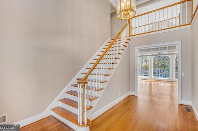 staircase with hardwood / wood-style flooring, a notable chandelier, and a high ceiling