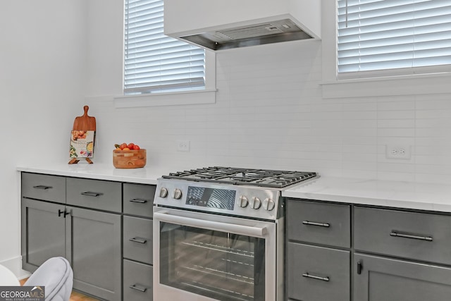 kitchen featuring backsplash, gray cabinets, exhaust hood, and high end stainless steel range oven