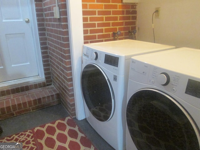 laundry area with separate washer and dryer and brick wall