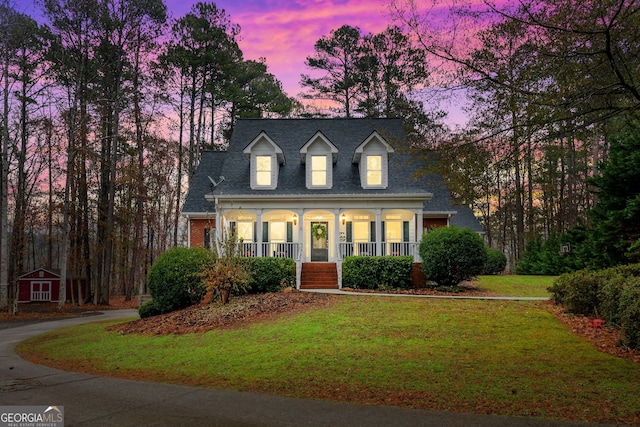 new england style home with a yard, covered porch, and a storage unit