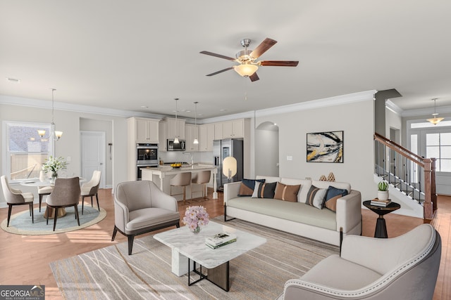 living room with ornamental molding, sink, ceiling fan with notable chandelier, and light hardwood / wood-style flooring