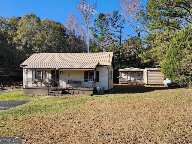 view of front of home with a front lawn, covered porch, central AC unit, and a storage shed