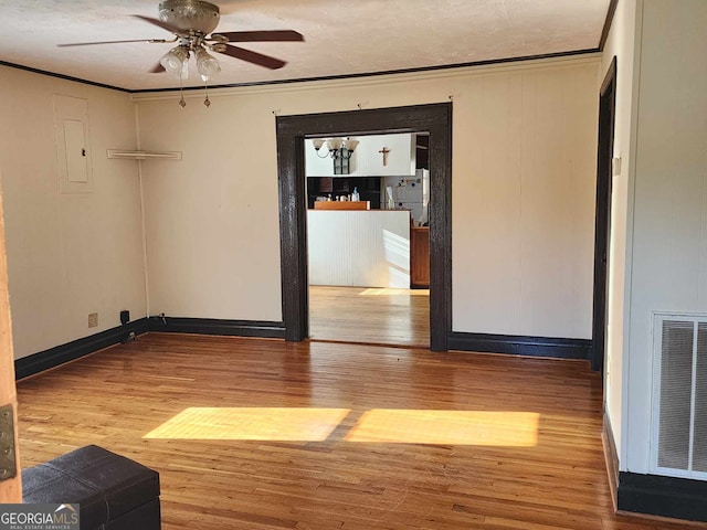 spare room featuring electric panel, crown molding, hardwood / wood-style floors, and ceiling fan with notable chandelier