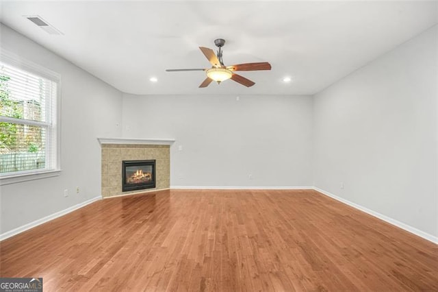 unfurnished living room with a tile fireplace, ceiling fan, and wood-type flooring