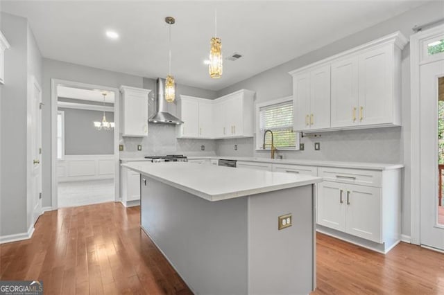 kitchen featuring a center island, white cabinetry, wall chimney range hood, and a wealth of natural light