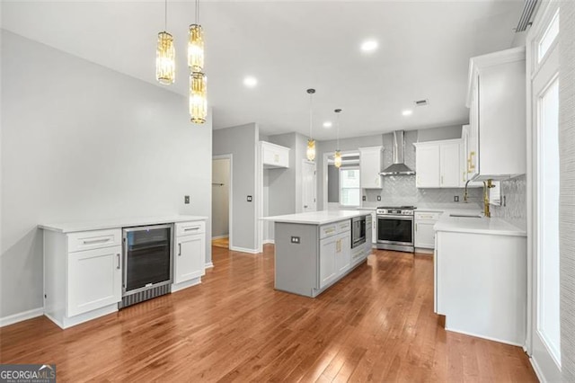 kitchen with white cabinets, a kitchen island, stainless steel appliances, and wall chimney range hood