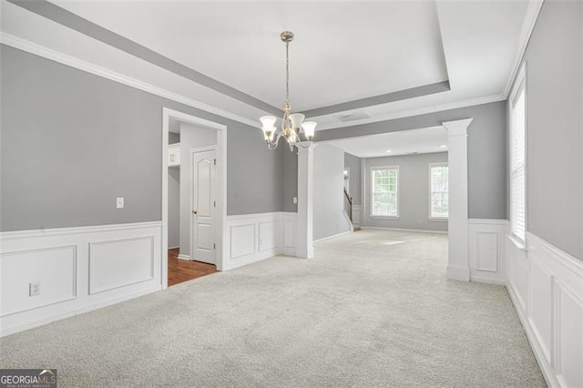 carpeted spare room with a notable chandelier, ornate columns, ornamental molding, and a tray ceiling