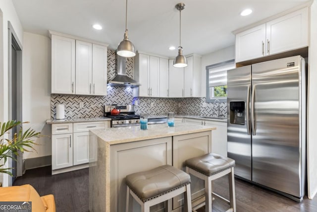 kitchen with pendant lighting, a breakfast bar, wall chimney exhaust hood, appliances with stainless steel finishes, and dark hardwood / wood-style flooring