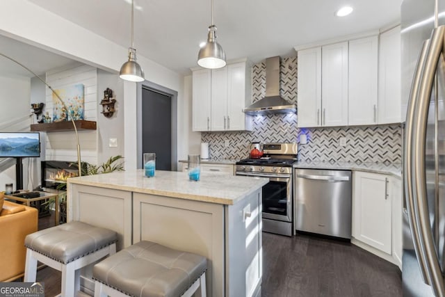 kitchen with appliances with stainless steel finishes, dark hardwood / wood-style flooring, light stone counters, wall chimney exhaust hood, and decorative light fixtures