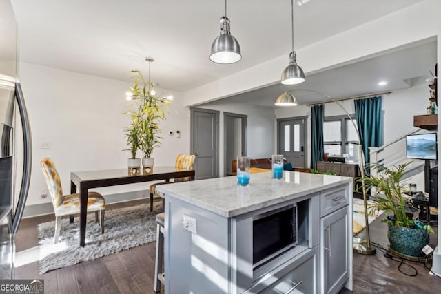 kitchen with light stone counters, stainless steel appliances, a center island, dark hardwood / wood-style floors, and hanging light fixtures