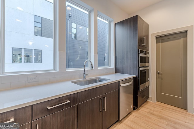 kitchen with dark brown cabinetry, sink, appliances with stainless steel finishes, and light hardwood / wood-style flooring