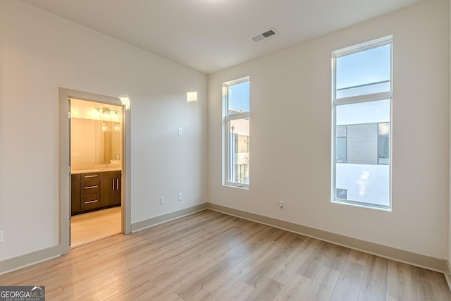 unfurnished bedroom featuring light hardwood / wood-style floors, multiple windows, and ensuite bathroom