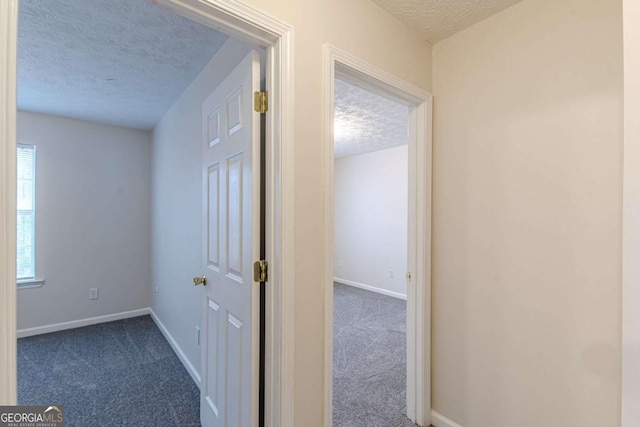 corridor with a textured ceiling and dark colored carpet