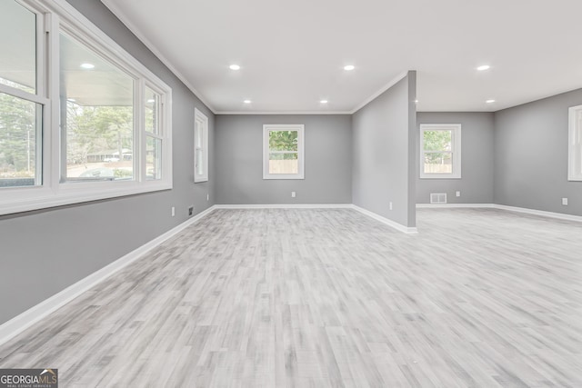 empty room with ornamental molding, plenty of natural light, and light hardwood / wood-style floors