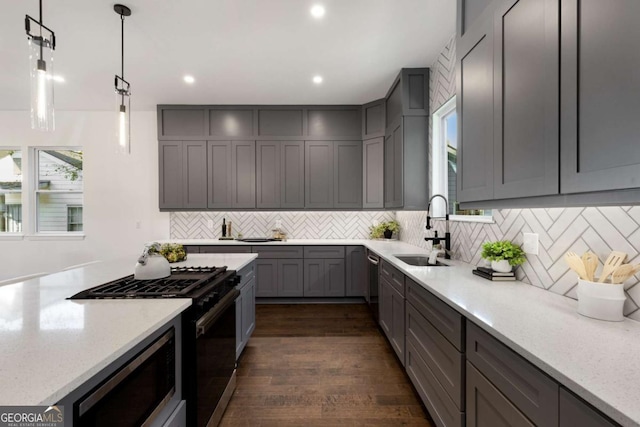 kitchen featuring dark wood-type flooring, sink, appliances with stainless steel finishes, decorative light fixtures, and light stone counters