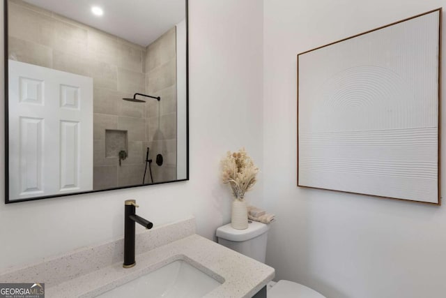 bathroom with vanity, toilet, and tiled shower