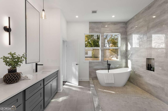 bathroom featuring tile patterned flooring, vanity, a tub to relax in, and tile walls