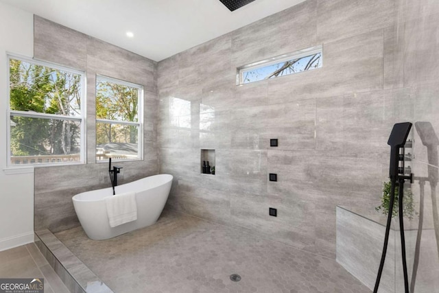 bathroom featuring tile patterned flooring, a bath, a wealth of natural light, and tile walls