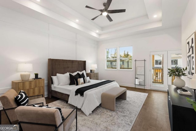 bedroom with ceiling fan, a towering ceiling, wood-type flooring, a tray ceiling, and access to outside