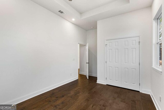 unfurnished bedroom featuring a tray ceiling, a closet, and dark wood-type flooring