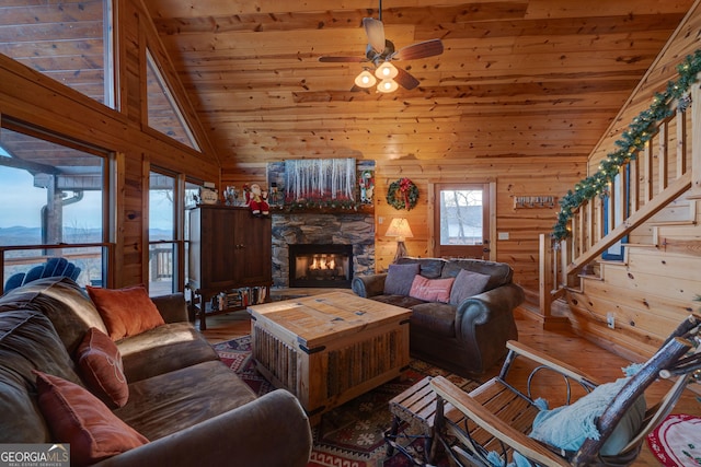 living room with ceiling fan, a stone fireplace, dark hardwood / wood-style flooring, high vaulted ceiling, and wood walls