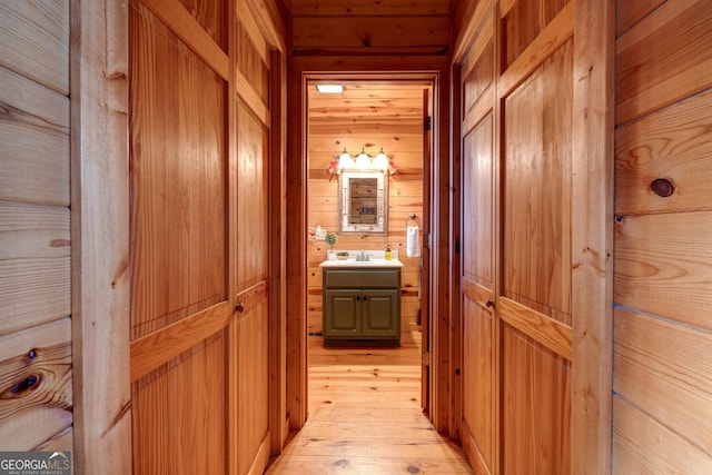 hall featuring sink, light hardwood / wood-style floors, and wood walls