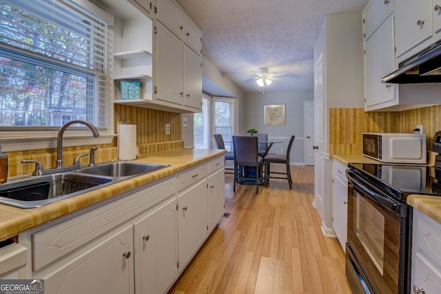 kitchen featuring sink, ceiling fan, black / electric stove, light hardwood / wood-style floors, and white cabinetry