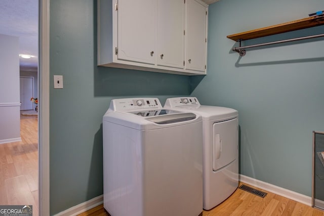 laundry room featuring cabinets, light wood-type flooring, and separate washer and dryer