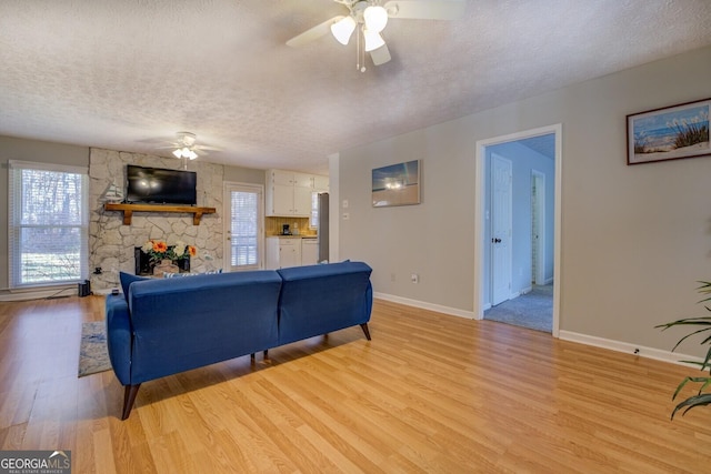 living room with ceiling fan, a fireplace, a textured ceiling, and light wood-type flooring