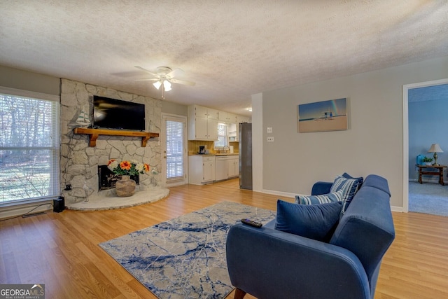 living room featuring a fireplace, a textured ceiling, light hardwood / wood-style floors, and ceiling fan