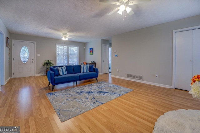 living room featuring ceiling fan, a textured ceiling, and light wood-type flooring