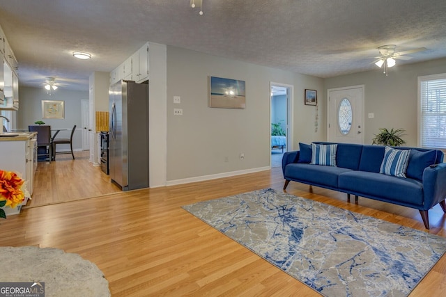 living room featuring ceiling fan, light hardwood / wood-style flooring, and a textured ceiling