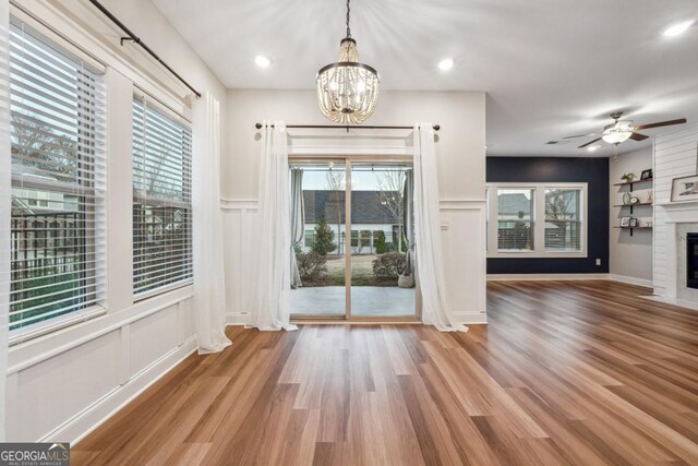 unfurnished dining area featuring a fireplace, hardwood / wood-style floors, and ceiling fan with notable chandelier