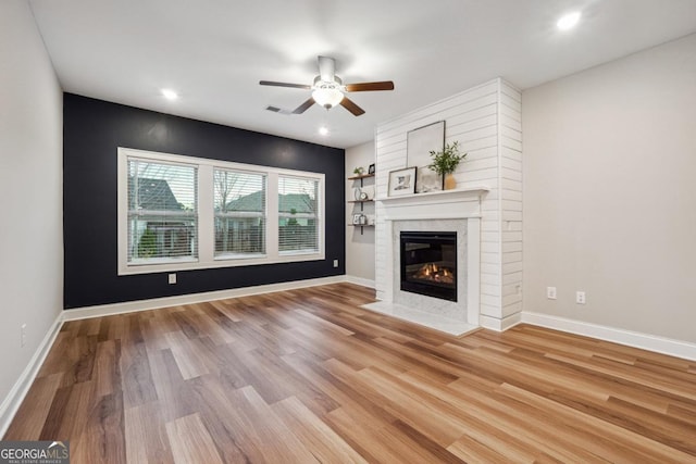 unfurnished living room with ceiling fan, a large fireplace, and light wood-type flooring