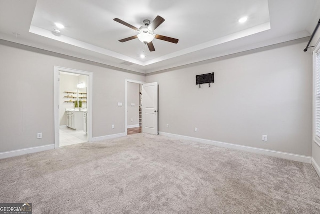 unfurnished bedroom featuring a raised ceiling, ensuite bathroom, ceiling fan, and light carpet