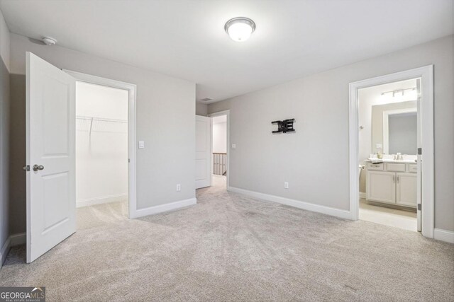 unfurnished bedroom featuring ensuite bath, sink, light colored carpet, a walk in closet, and a closet