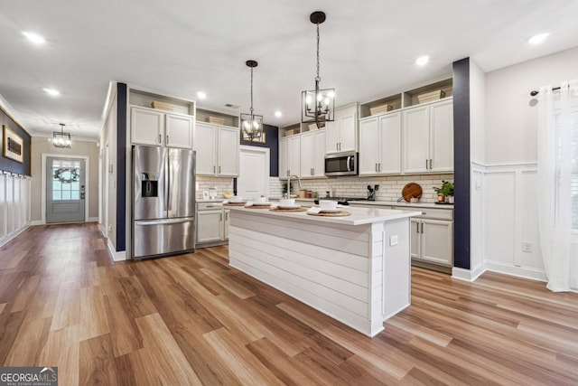 kitchen with white cabinetry, light hardwood / wood-style floors, decorative light fixtures, a kitchen island with sink, and appliances with stainless steel finishes