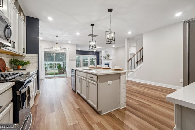 kitchen with a kitchen island with sink, sink, hanging light fixtures, decorative backsplash, and stainless steel appliances