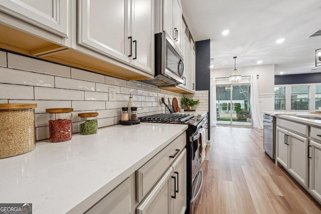 kitchen featuring light stone countertops, stainless steel appliances, pendant lighting, decorative backsplash, and light wood-type flooring