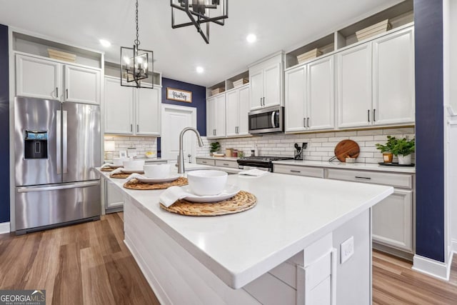 kitchen featuring appliances with stainless steel finishes, backsplash, light hardwood / wood-style floors, white cabinetry, and an island with sink