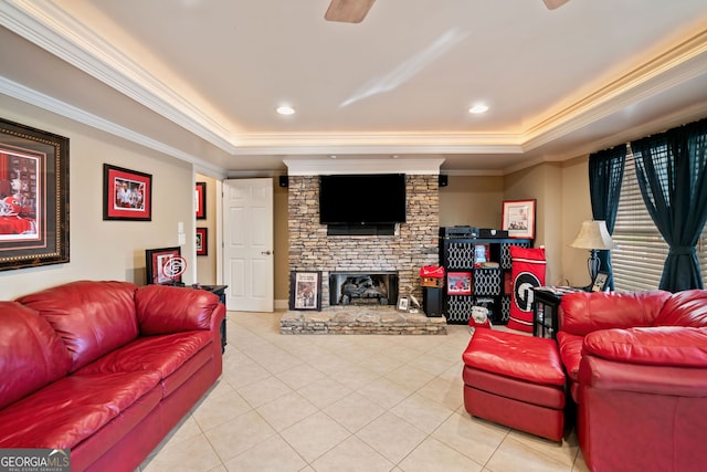 living room featuring a tray ceiling, light tile patterned floors, ornamental molding, a stone fireplace, and a ceiling fan